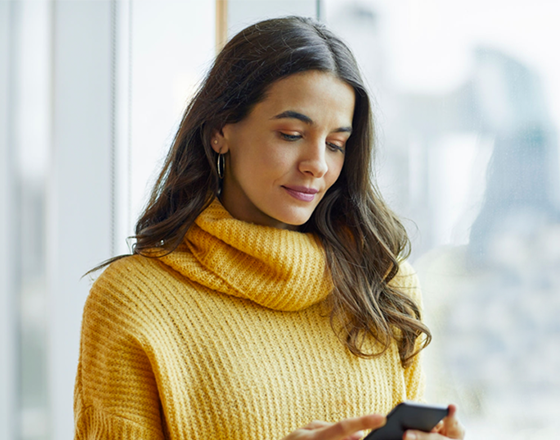 woman in yellow turtleneck looking at phone